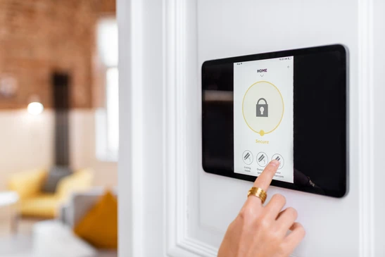 Une main tient un smartphone affichant une interface "SMART HOME" avec des icônes de domotique (éclairage, sécurité, paramètres) au-dessus d'un clavier d'ordinateur portable