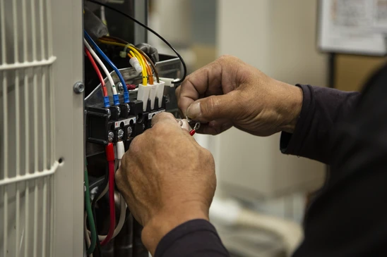 Électricien en uniforme professionnel intervenant d'urgence chez un client, en train de diagnostiquer ou réparer un problème électrique sur un panneau électrique ou une installation murale défaillante. L'électricien porte son équipement de travail professionnel et tient ses outils de diagnostic. La scène se déroule dans un intérieur résidentiel ou professionnel, montrant clairement l'urgence et la réactivité de l'intervention, avec une expression concentrée du professionnel en plein travail de dépannage.